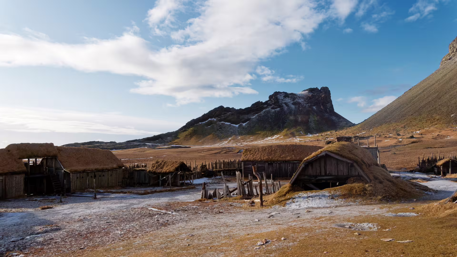 Authentic Viking Age settlement with grass-roofed structures and dramatic Iceland mountain backdrop