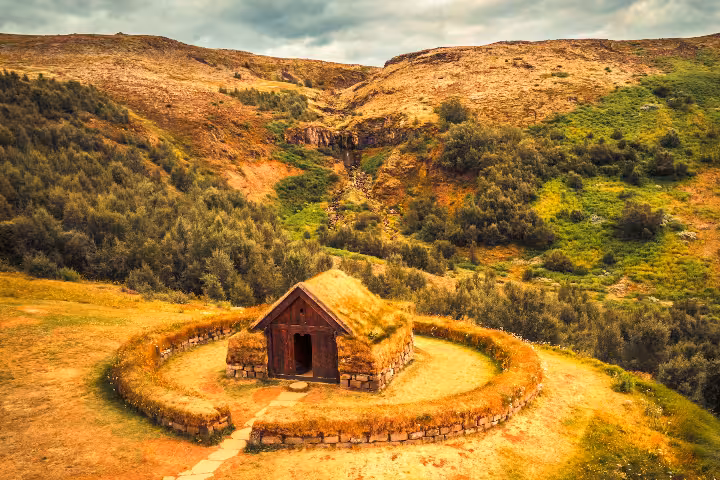 Aerial view of ancient Viking turf longhouse nestled in lush Iceland valley on South Coast summer adventure tour