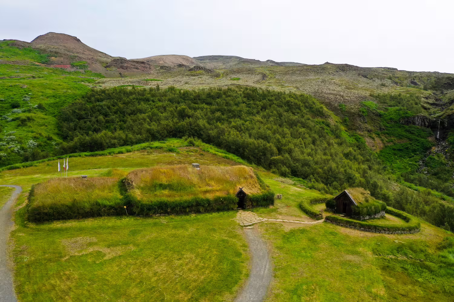 Aerial view of ancient Viking turf longhouse with grass roof nestled in lush Icelandic valley on Celtic heritage tour