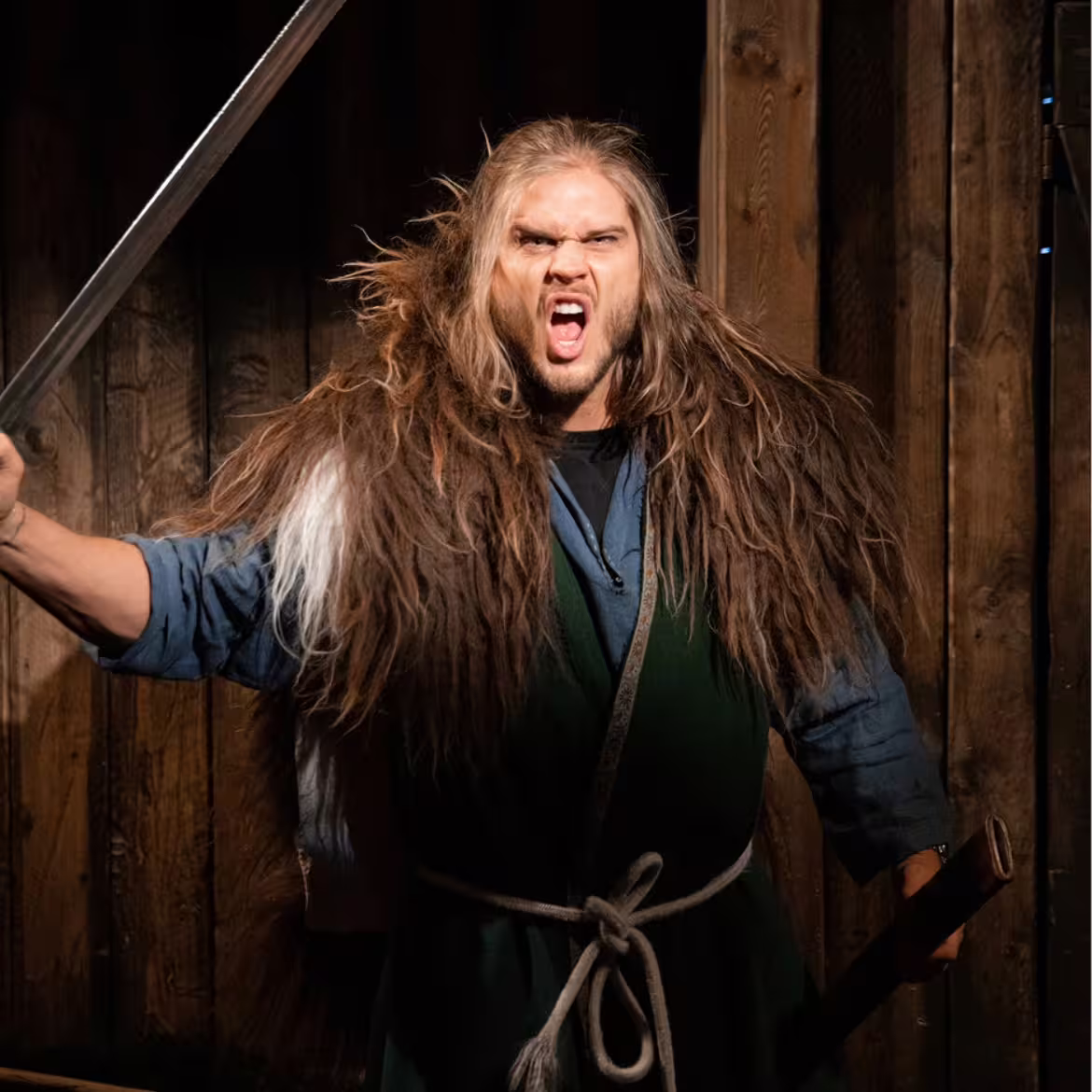 Viking warrior actor with long hair wielding sword at Skagafjordur turf museum living history tour