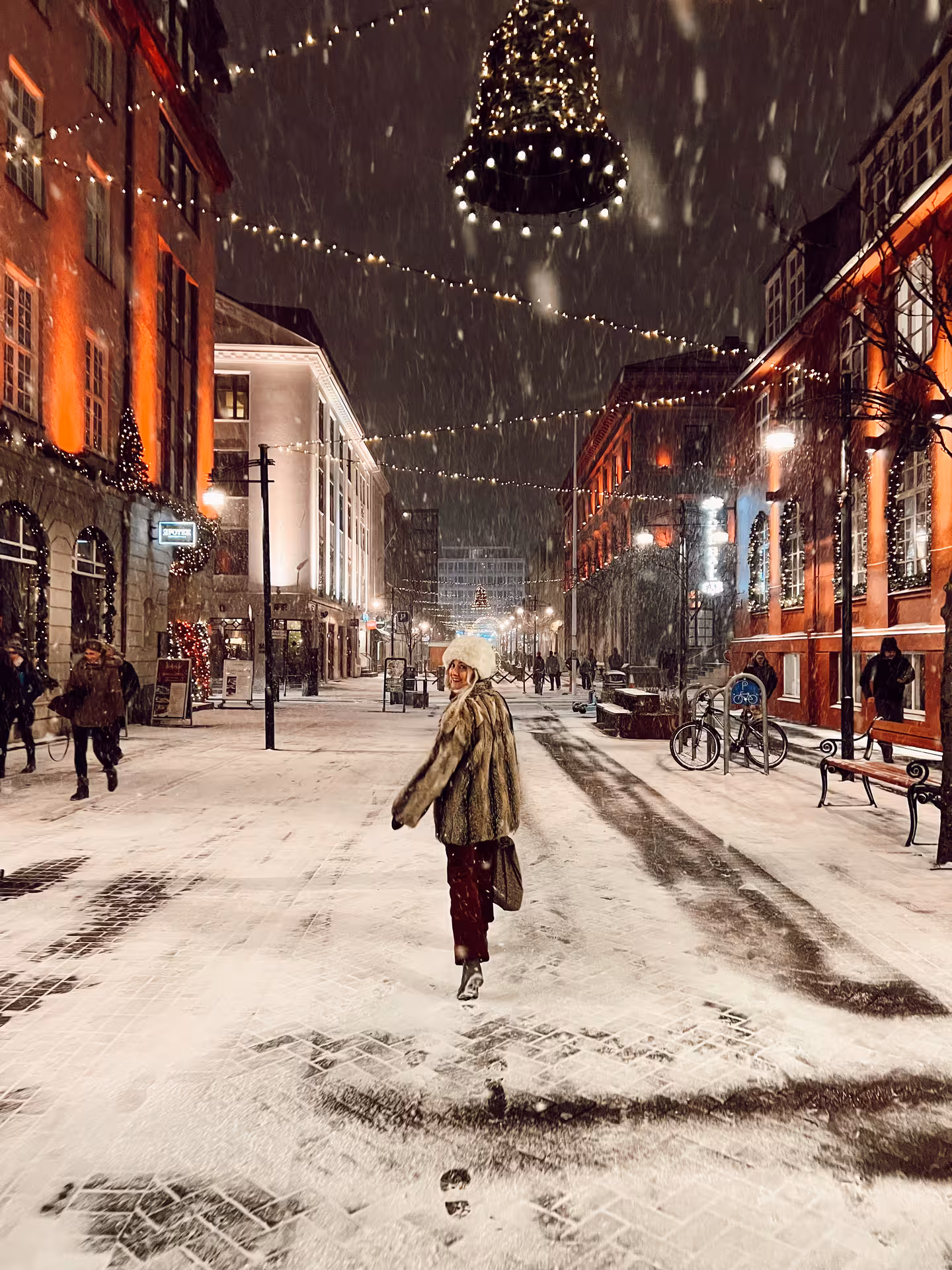 Woman exploring a festive, snowy city street adorned with twinkling lights during a Viking winter adventure.