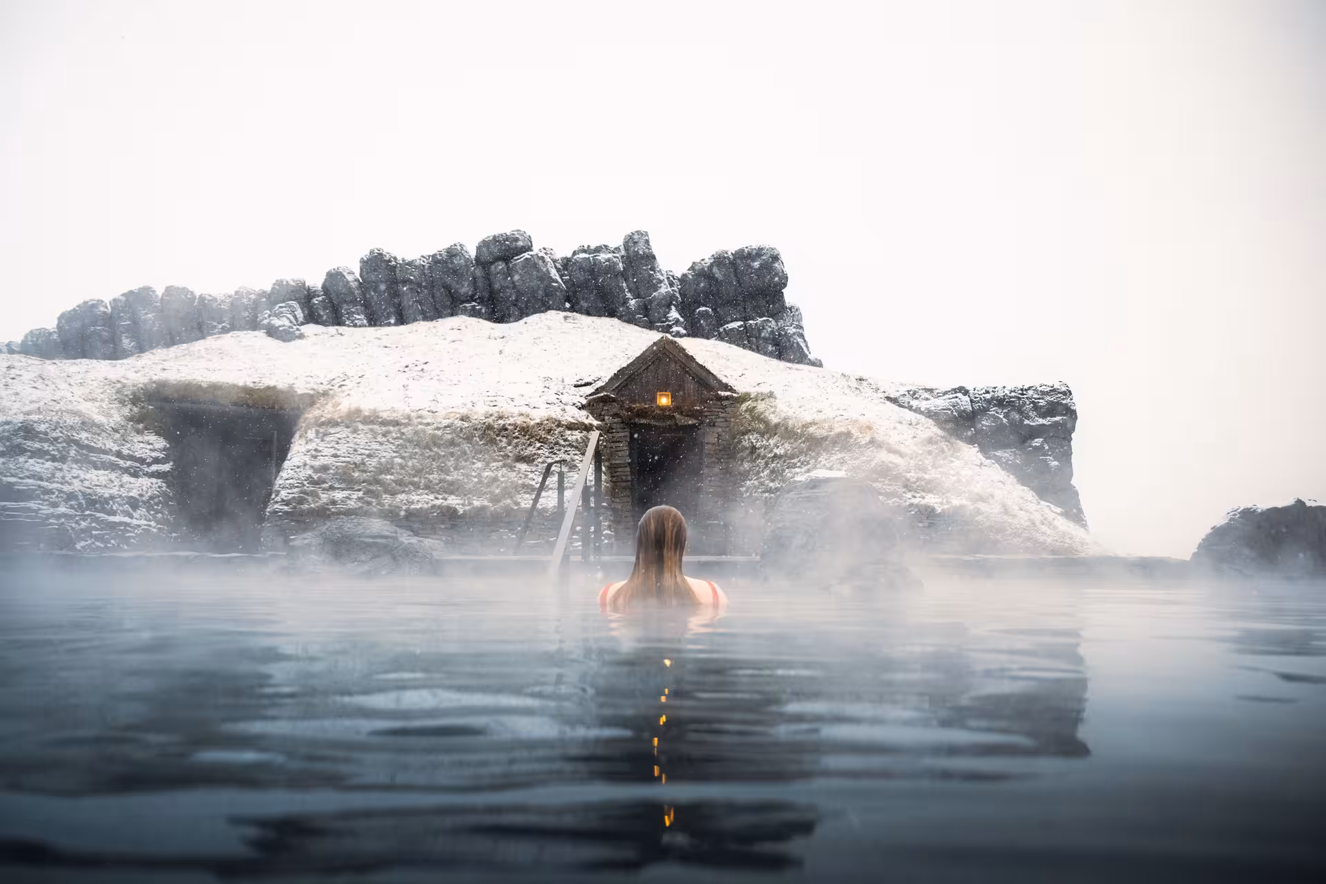Woman enjoying a serene hot spring surrounded by snow, in a remote, scenic location on a women-only Viking tour.