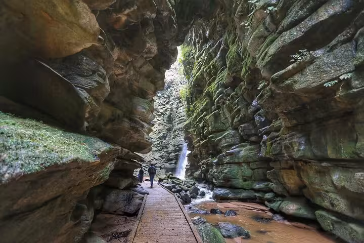 Stunning rock formations and a waterfall along a wooden path in Buraco do Padre, ideal for adventure seekers.