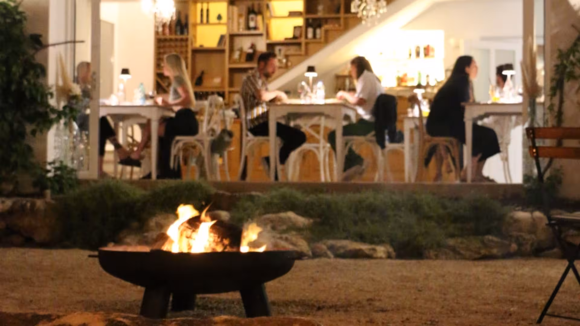 Cozy indoor dining scene with guests enjoying a meal around a warm fire pit in a serene villa setting.