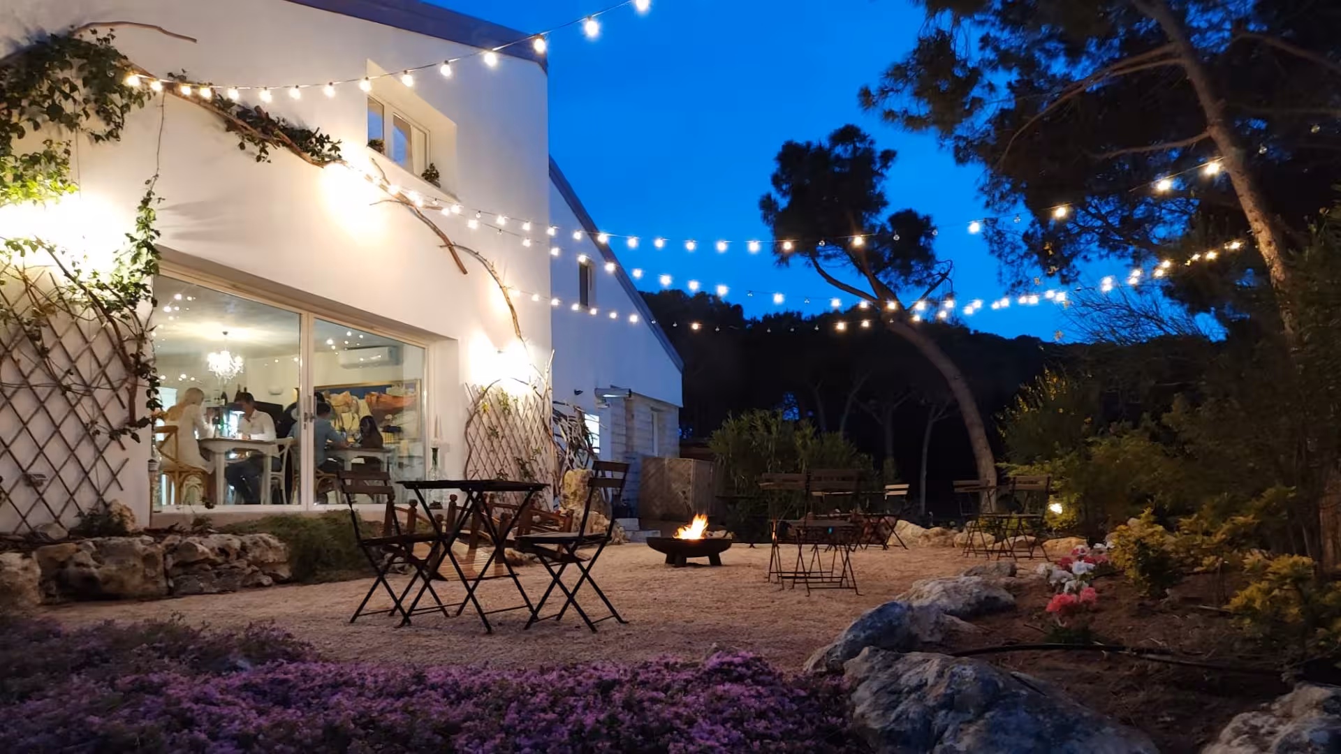 Enchanting villa garden at dusk with string lights, cozy seating, and a fire pit for a relaxing evening with dinner.