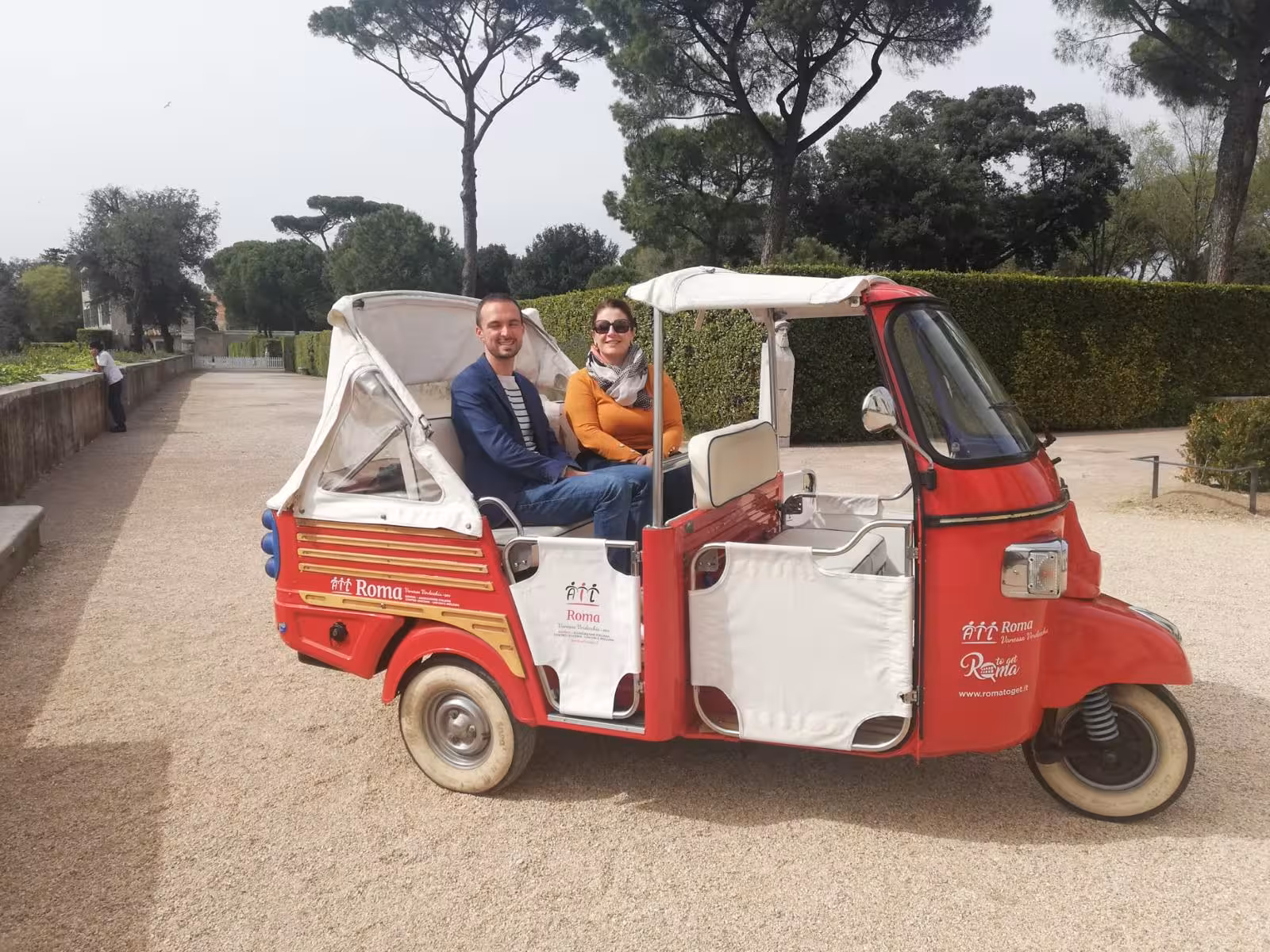 Couple enjoying a Villa Medici Combo Tour ride in a red tuk-tuk amidst lush Roman gardens.
