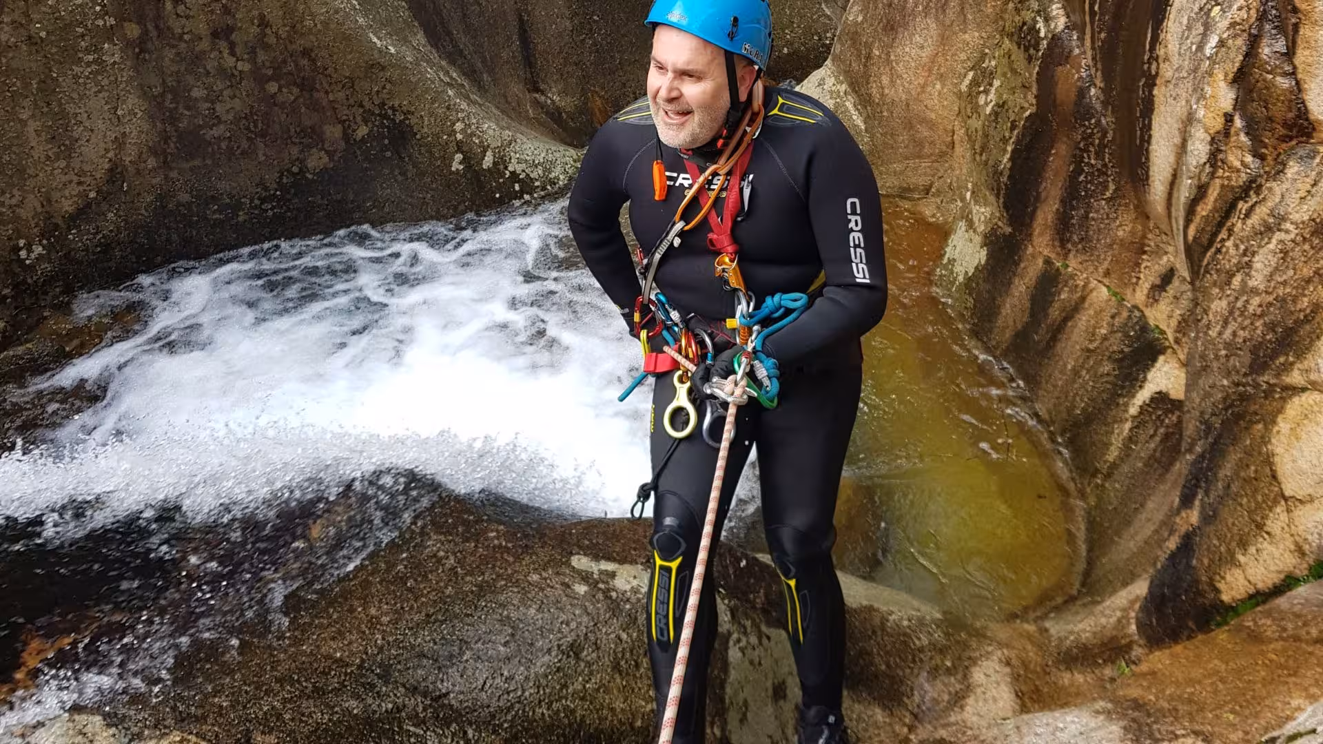 Smiling man in helmet and wetsuit rappelling in the scenic Rio Zairi canyon, Villacidro, Sardinia.