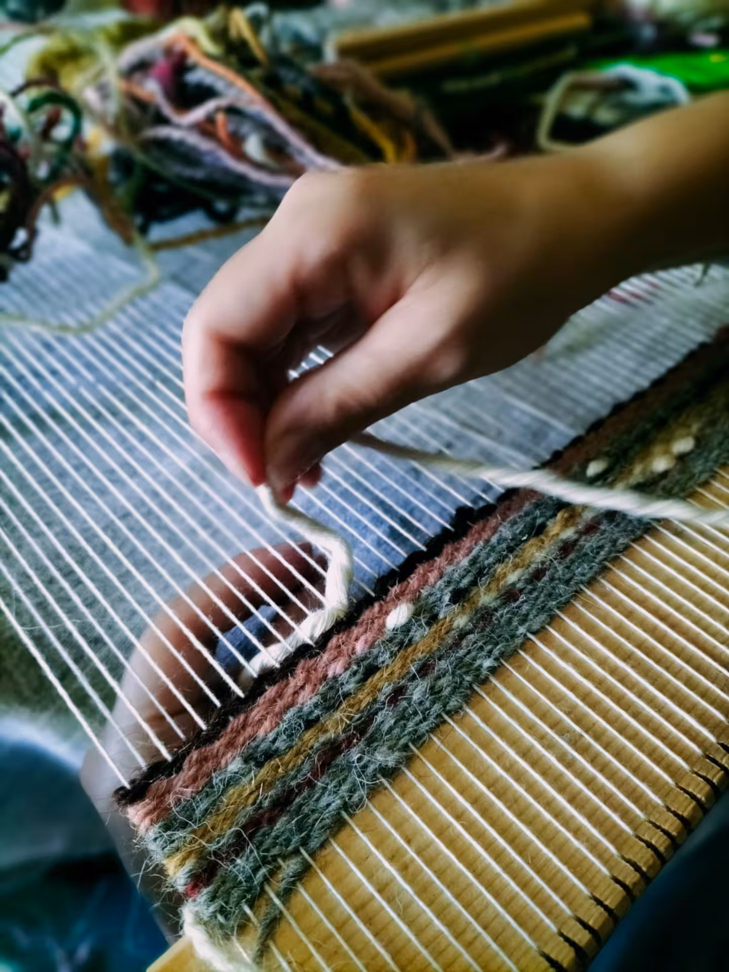 Hands weaving colorful threads on a loom at Villacidro workshop, illustrating Sardinian textile craftsmanship in action.