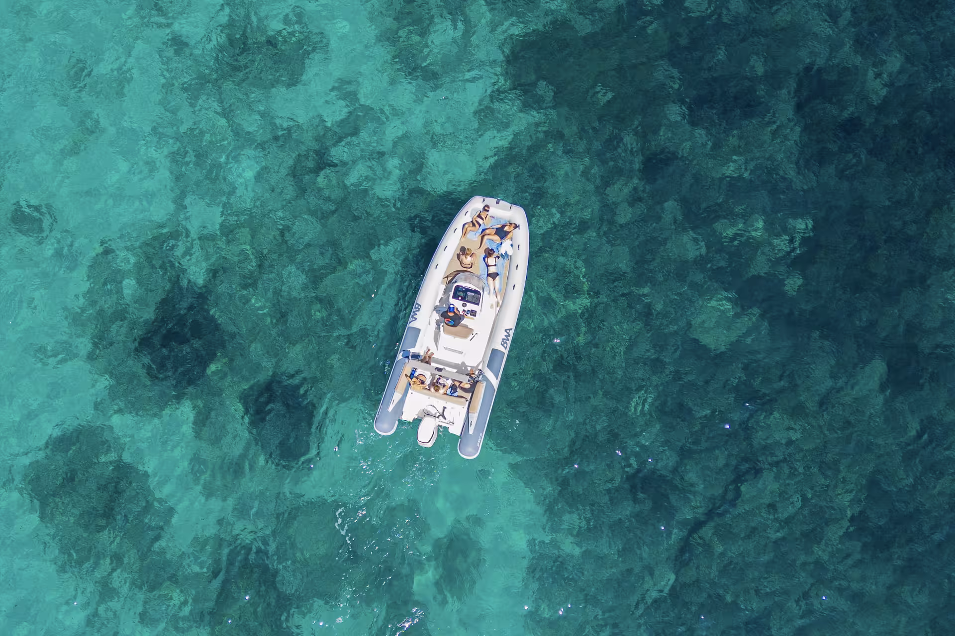 Top view of a RIB boat with passengers relaxing over vibrant green waters during Villasimius snorkeling tour.