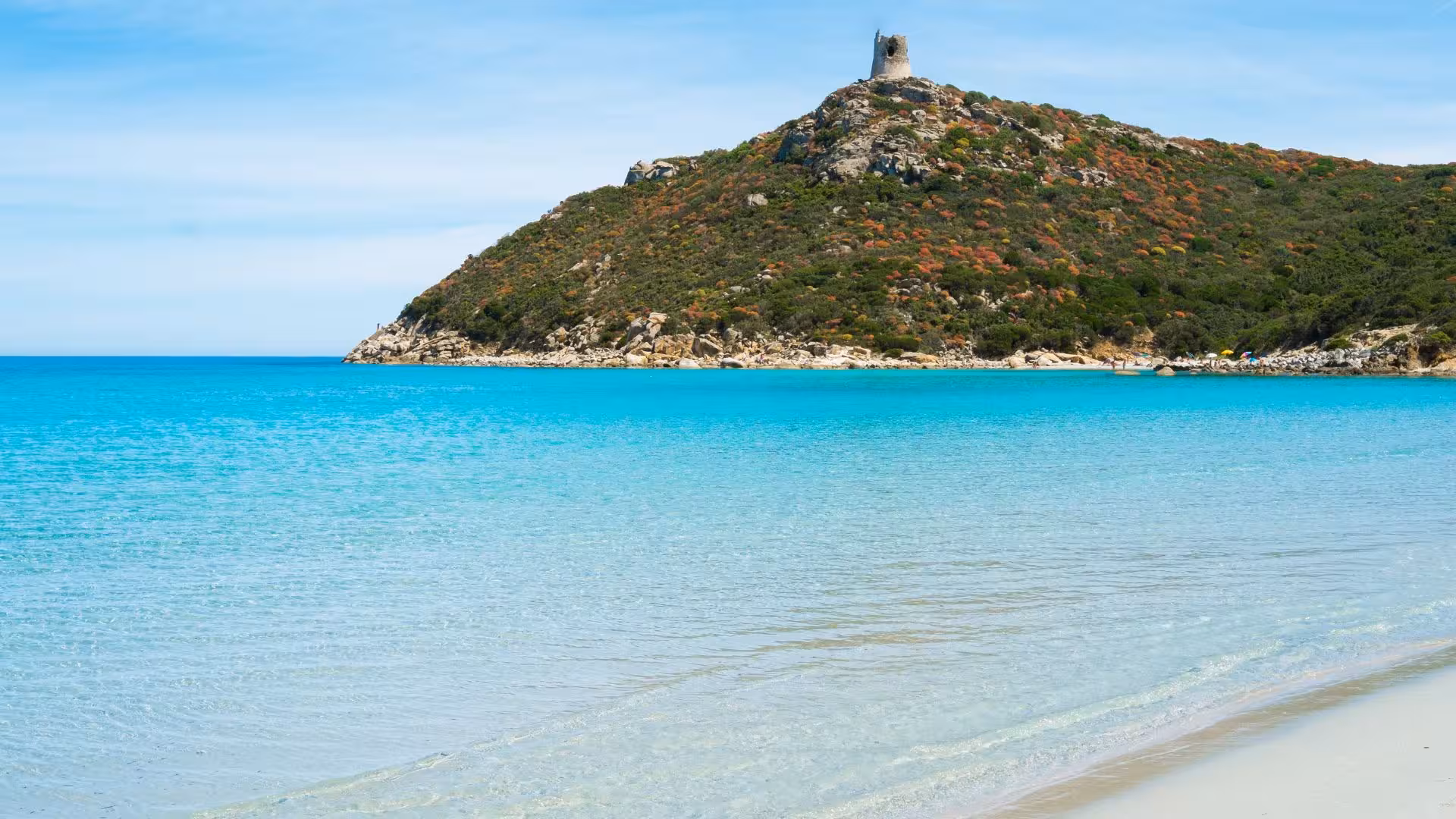 Scenic view of crystal-clear waters and ancient tower on a hillside in Villasimius, perfect for exploration.