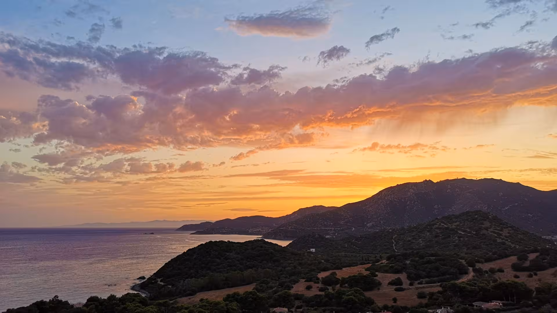 Breathtaking sunset over the Sardinian coastline, featuring dramatic clouds and lush hills.