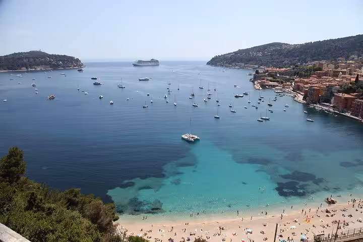 Aerial view of Villefranche-sur-Mer bay with turquoise water, sailboats, cruise ship, and beach near Nice