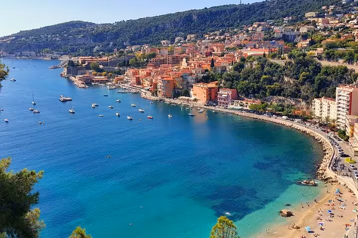 Aerial view of Villefranche-sur-Mer bay with turquoise waters, colorful old town buildings, and sandy beach on French Riviera