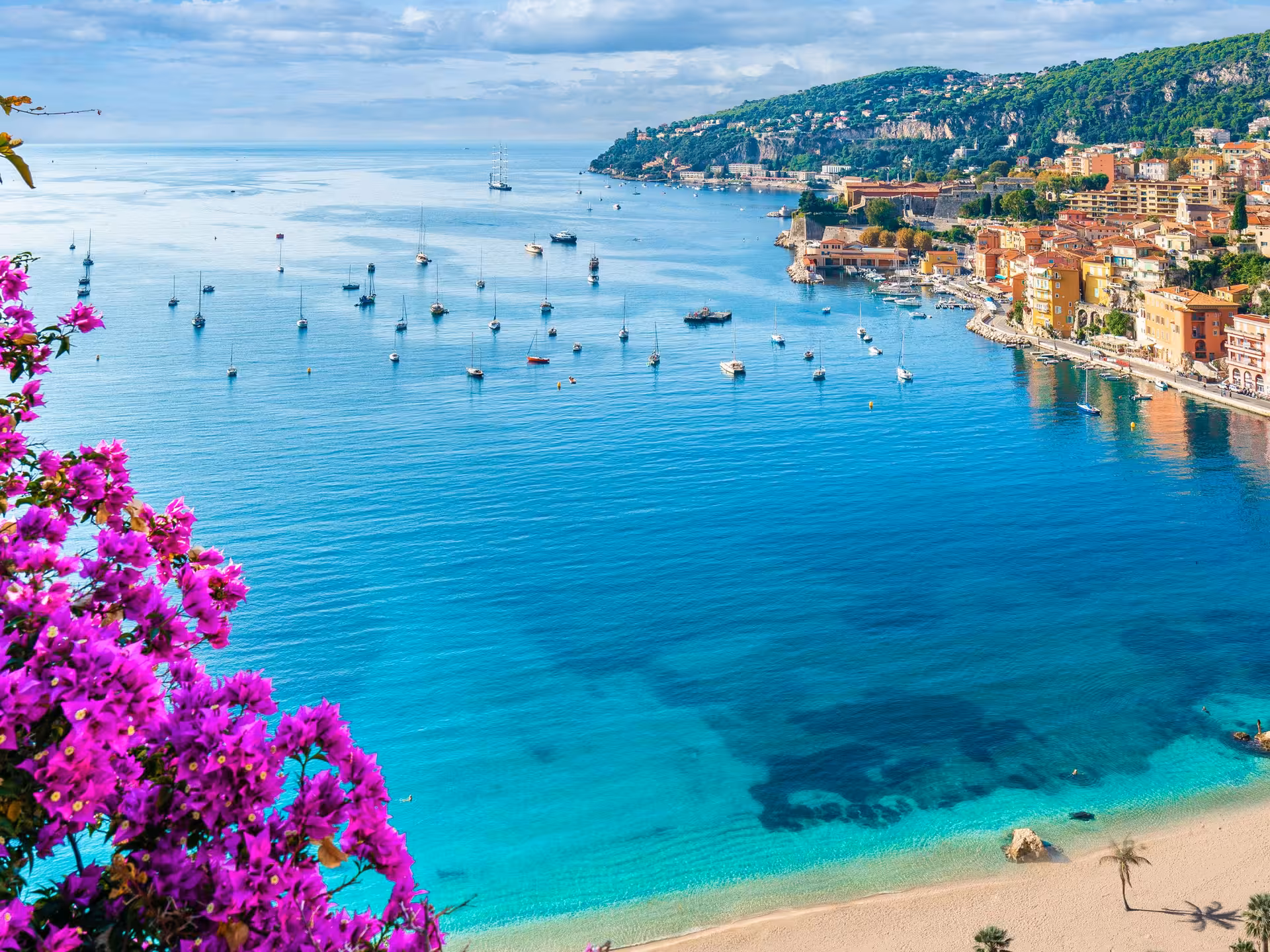 Turquoise bay of Villefranche-sur-Mer with sailboats, colorful waterfront buildings, and pink bougainvillea near Nice