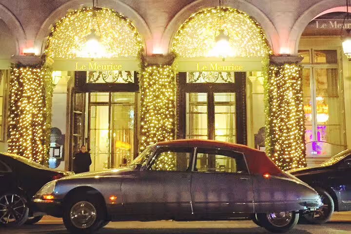 Vintage Citroën DS parked outside Le Meurice hotel in Paris at night, adorned with festive golden lights