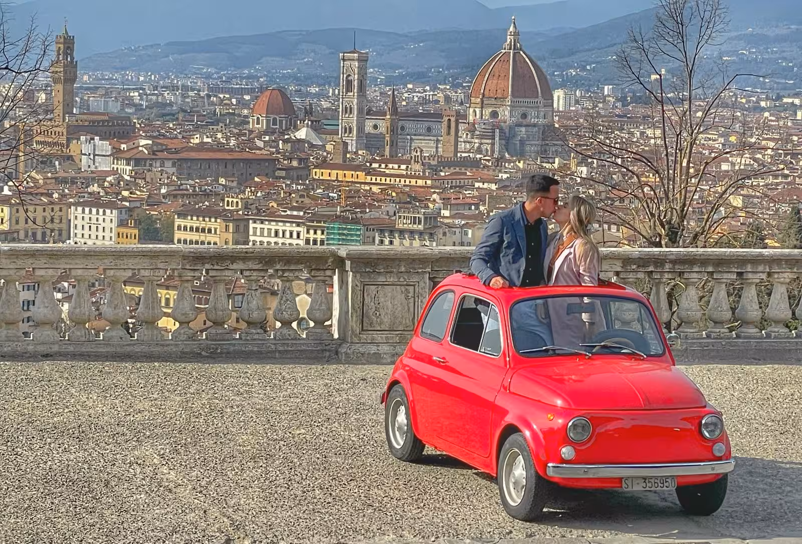 Couple embracing beside a red vintage FIAT 500 with stunning Florence skyline in the background.