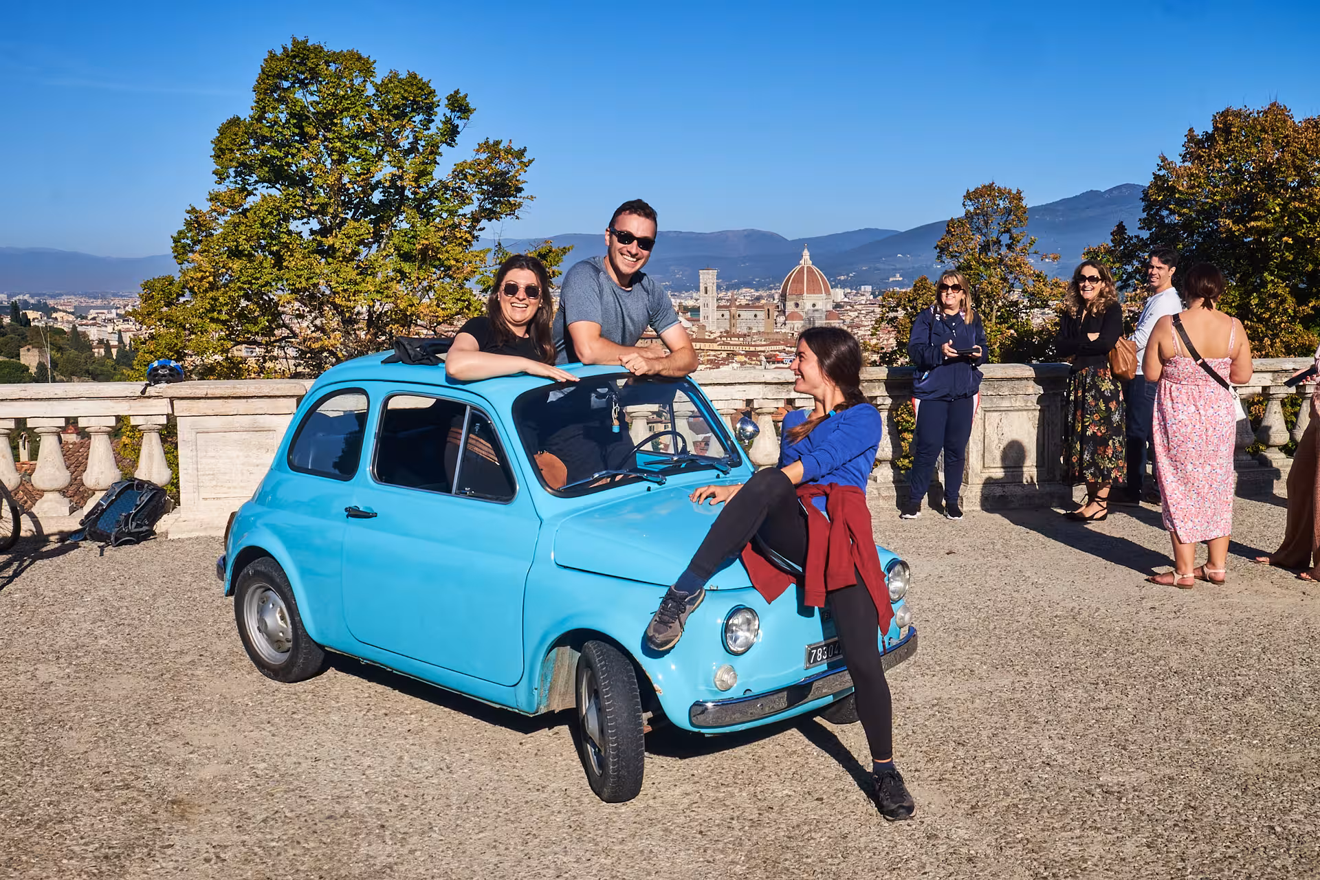 Friends posing with a blue vintage Fiat 500 overlooking Florence's stunning skyline.