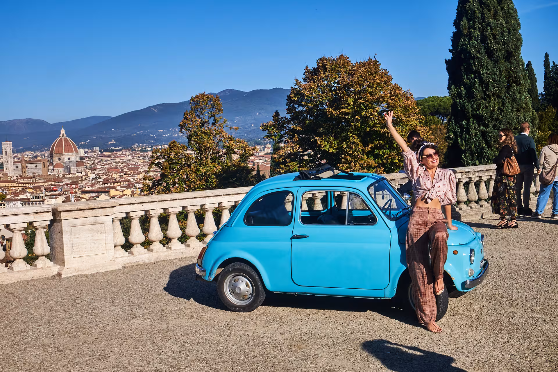 Tourist enjoying a scenic view of Florence from a classic blue FIAT 500 during a Tuscany olive oil tasting tour.