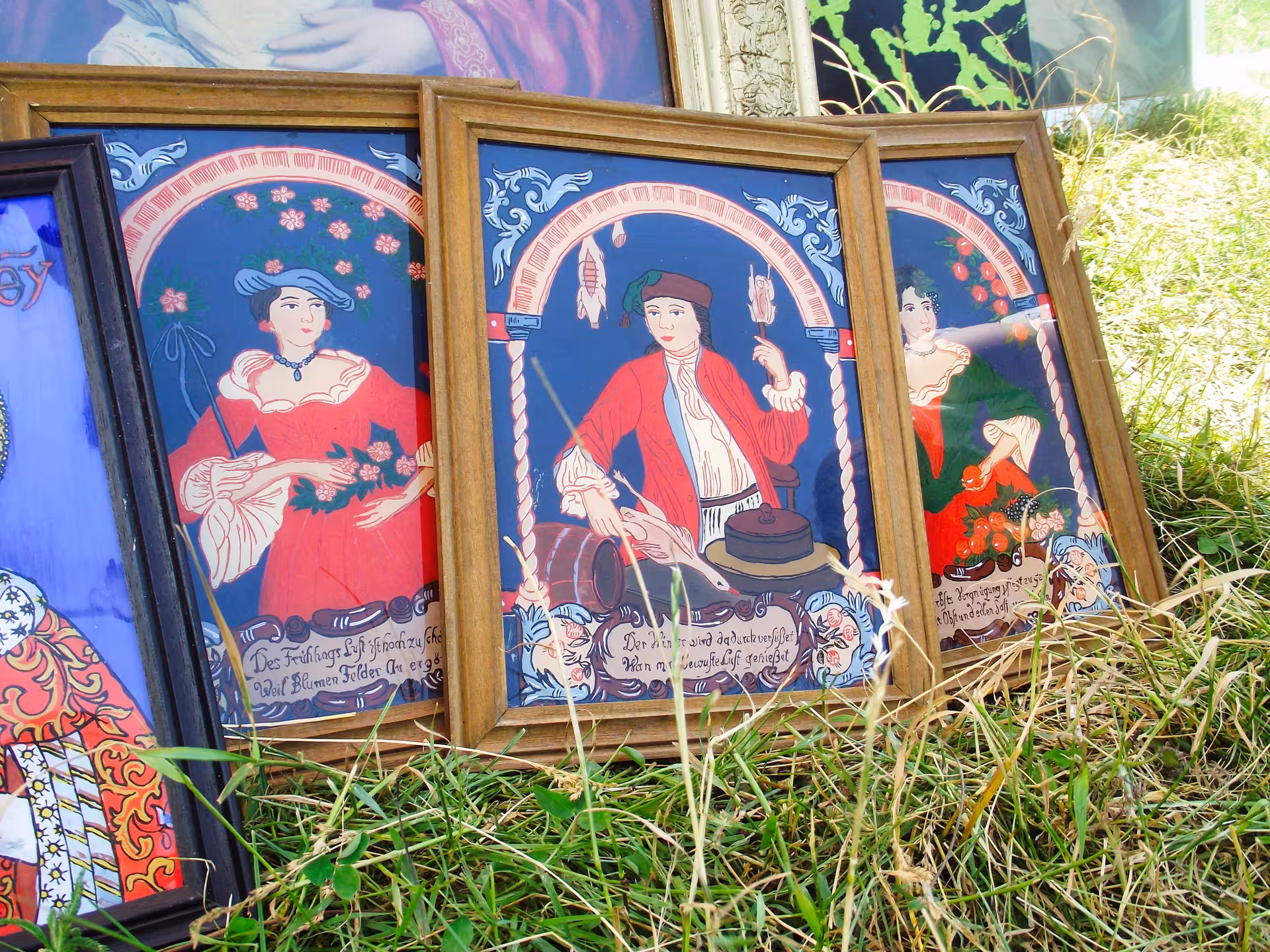 Vintage framed folk art paintings with German script displayed on grass at Negreni antique flea market guided tour