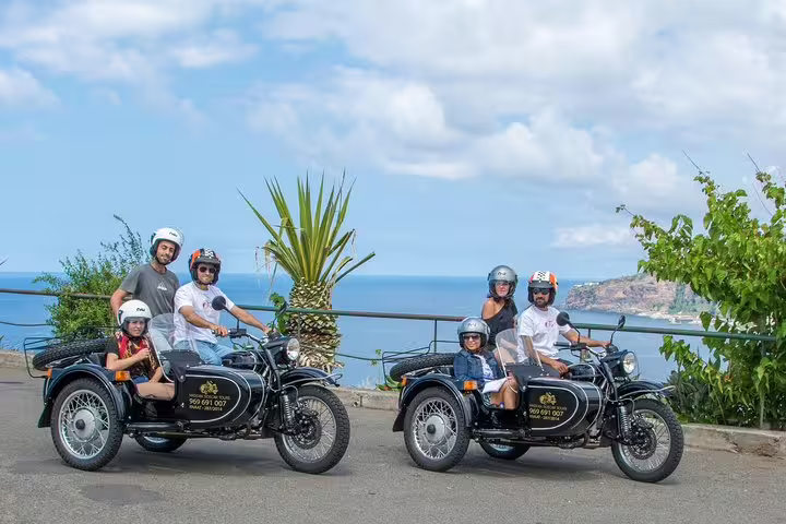 Two vintage sidecars with tourists and drivers enjoy a scenic coastal view during a Funchal city tour adventure.