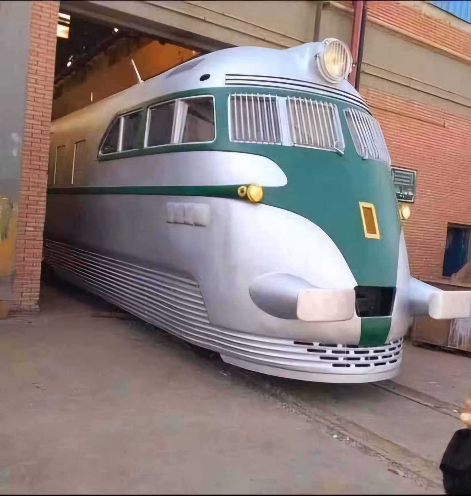 Vintage streamlined silver and green train locomotive emerging from a brick building