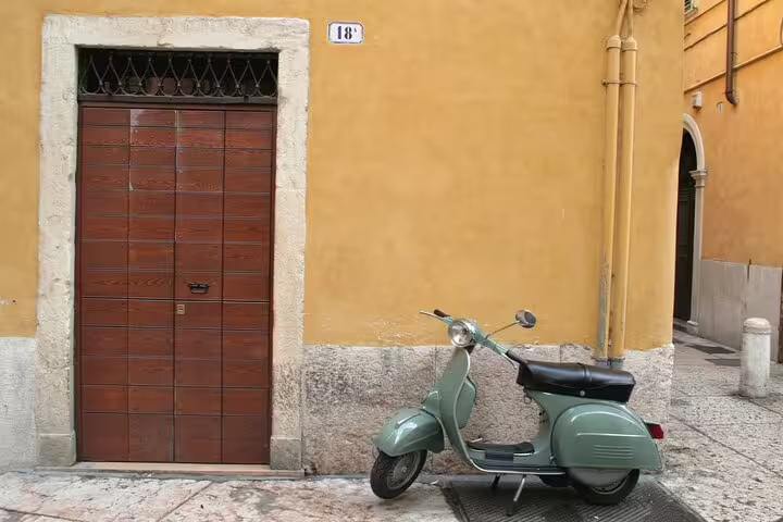 Vintage green Vespa scooter parked beside a yellow ochre building with wooden door in Rome