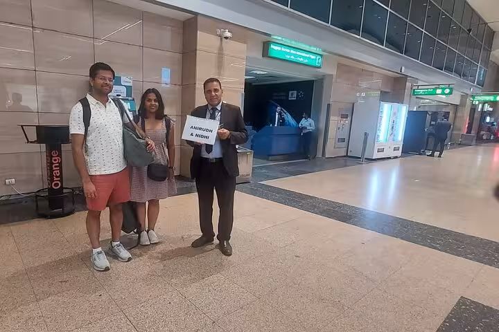 Couple welcomed by VIP airport assistant at Cairo with personalized sign, highlighting stress-free arrival service.