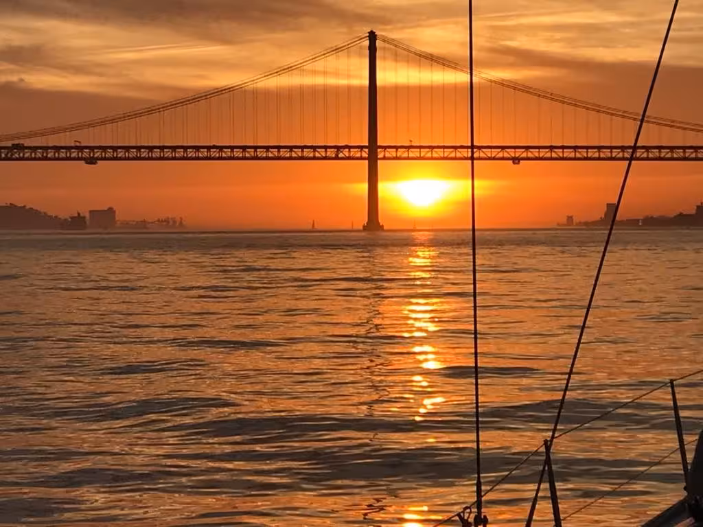 Sunset view from VIP catamaran sailing tour, golden reflections on the sea beneath a suspension bridge