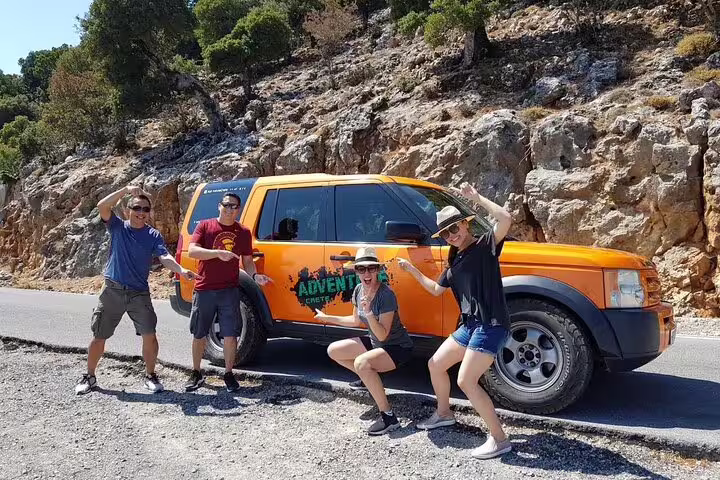 Excited tourists pose by an orange LandRover on a scenic mountain road, highlighting the VIP Luxury 4x4 tour experience.
