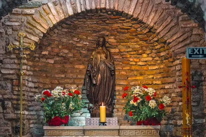 Statue of Virgin Mary surrounded by flowers in a stone alcove, part of the 7 Churches of Revelation tour.