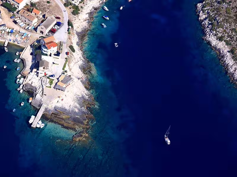 Aerial coastline near Vis with sailboat on deep blue Adriatic, scenic route on Vis and Hvar Blue Cave tour