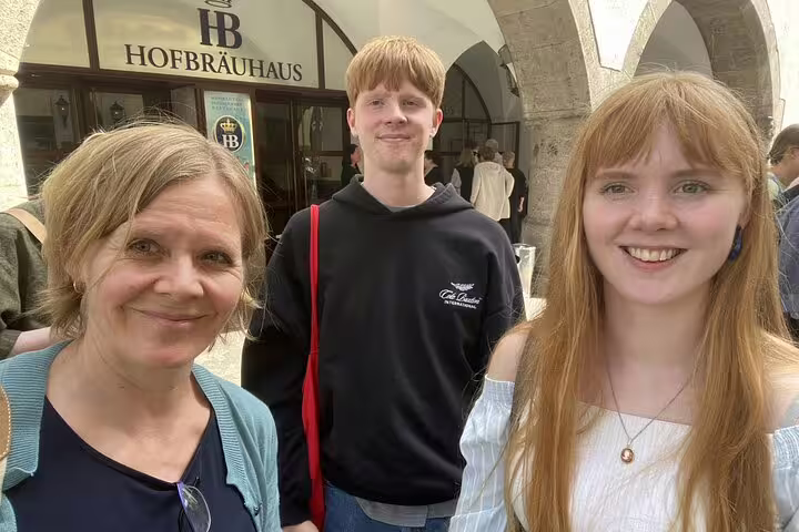 Three smiling visitors posing outside the historic Hofbräuhaus in Munich Old Town
