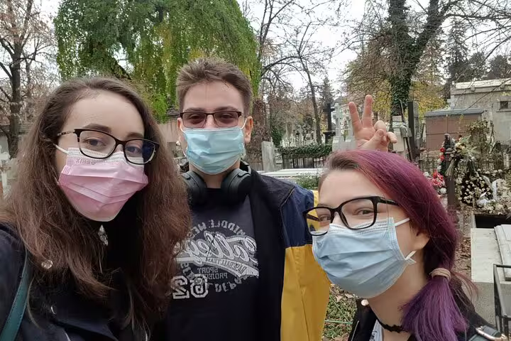Three young visitors wearing face masks taking a selfie at Bellu Cemetery Bucharest during a self-guided walking tour