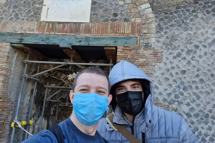 Two tourists wearing face masks posing for selfie at ancient Pompeii ruins entrance