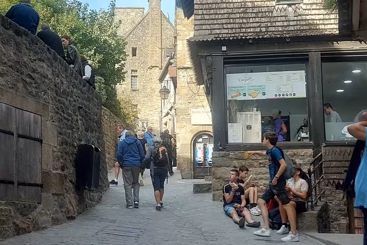 Visitors walking Mont Saint Michel medieval village street, a stop on small group luxury van day tour from Paris