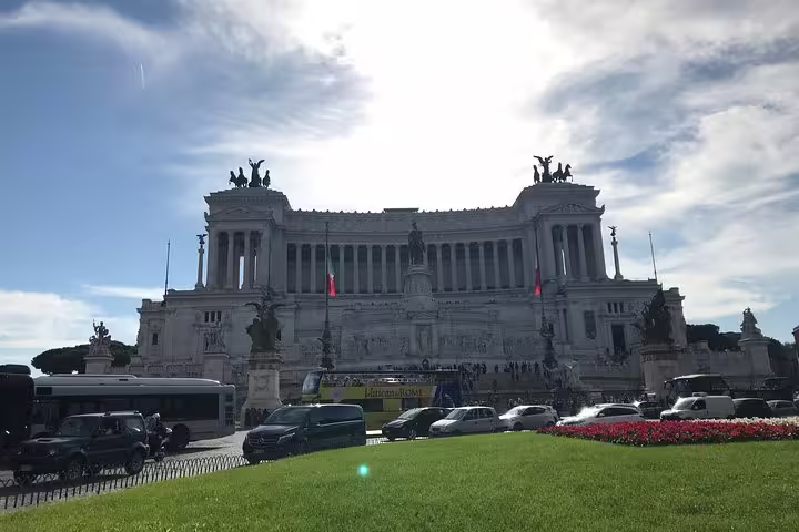 Vittoriano monument in Rome with traffic and red flowers in foreground under blue sky