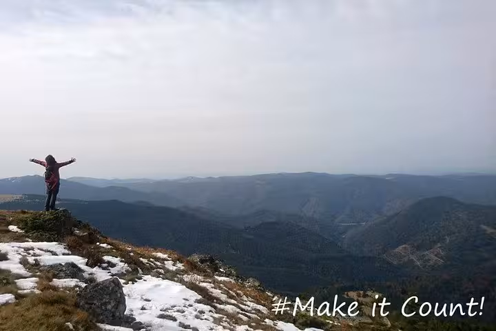 Hiker with arms outstretched on Vladeasa Peak summit overlooking snowy Apuseni mountain valleys