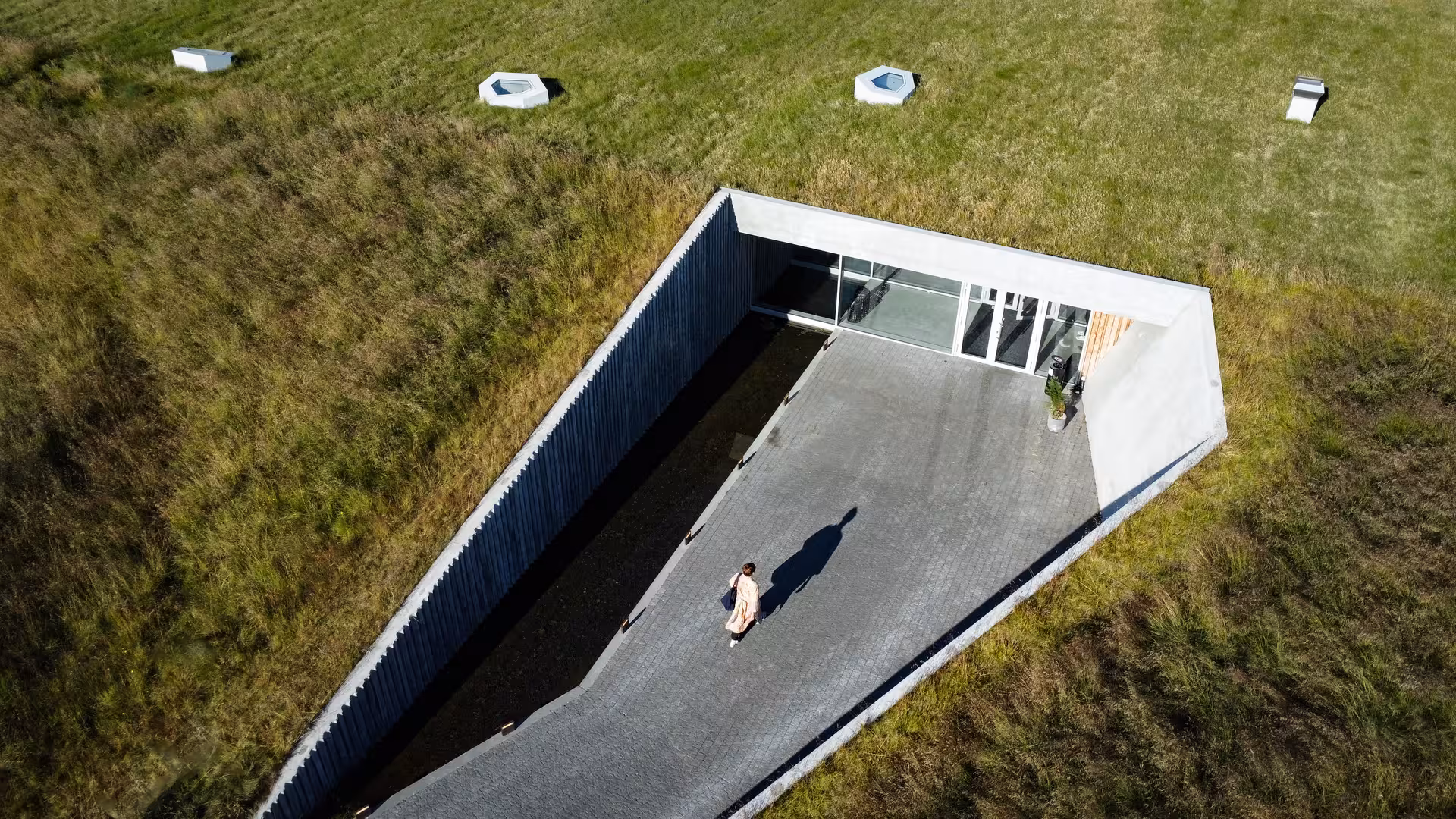 Aerial view of Vok Baths sunken entrance pathway with grass roof and skylights in Eastfjords Iceland