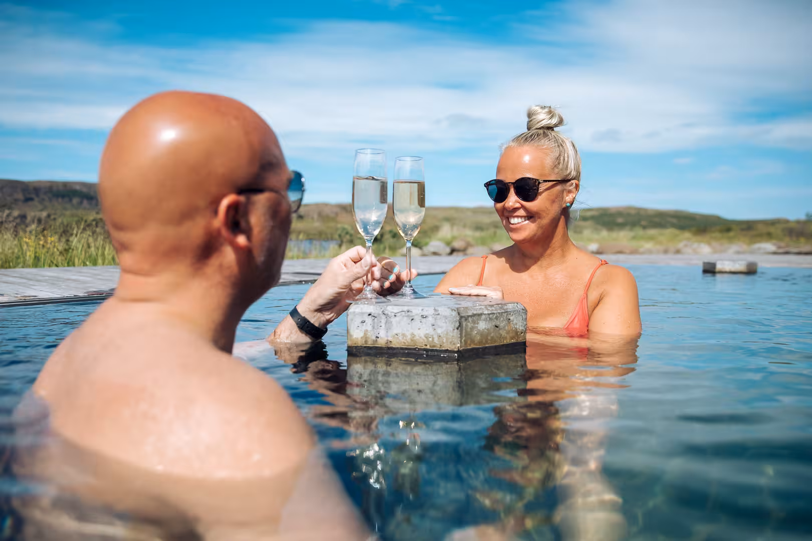 Couple toasting with champagne flutes in the geothermal Vok Baths pool, East Iceland on a sunny day