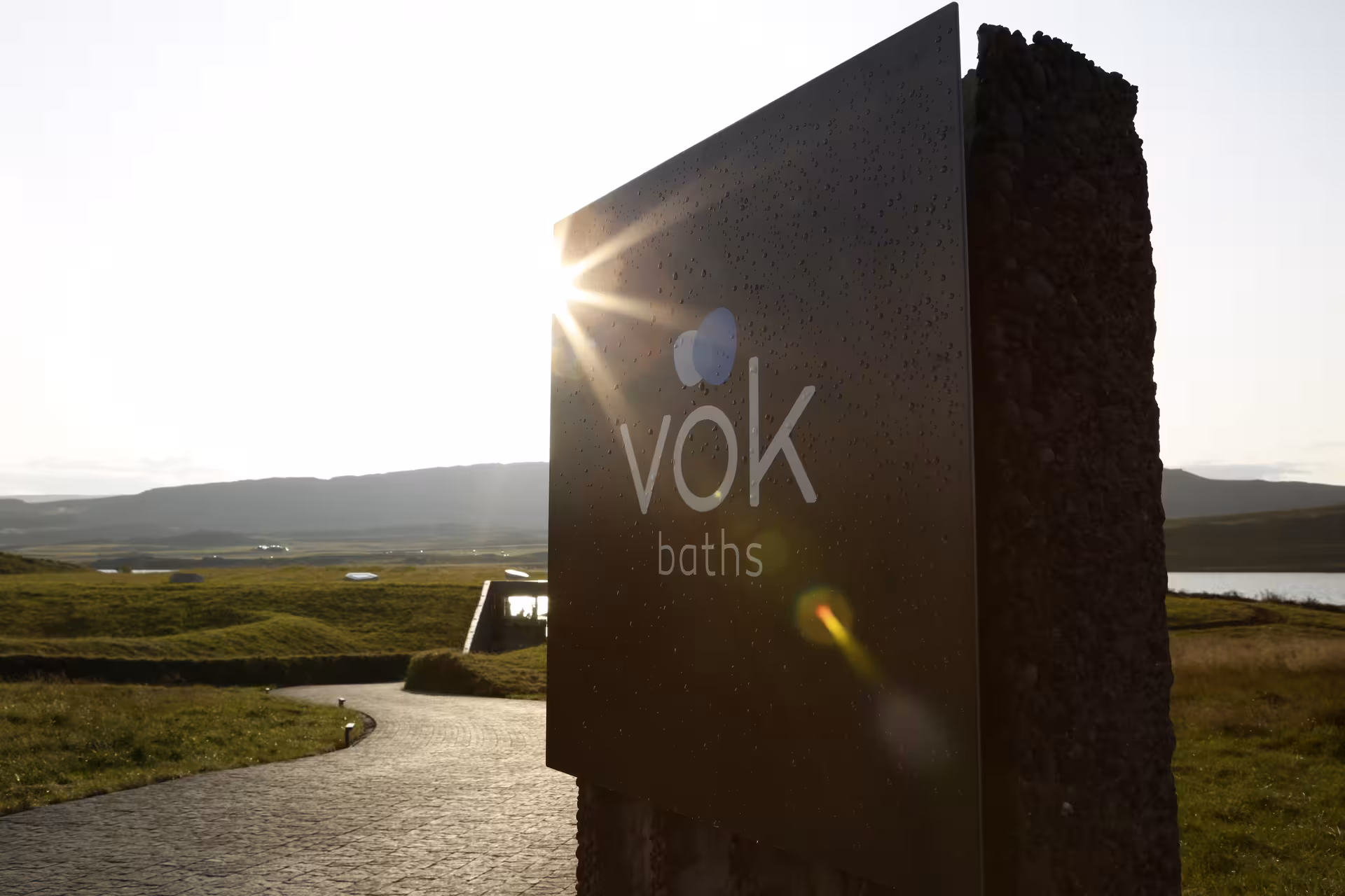 Vok Baths entrance sign at golden hour with Icelandic landscape and lake in background