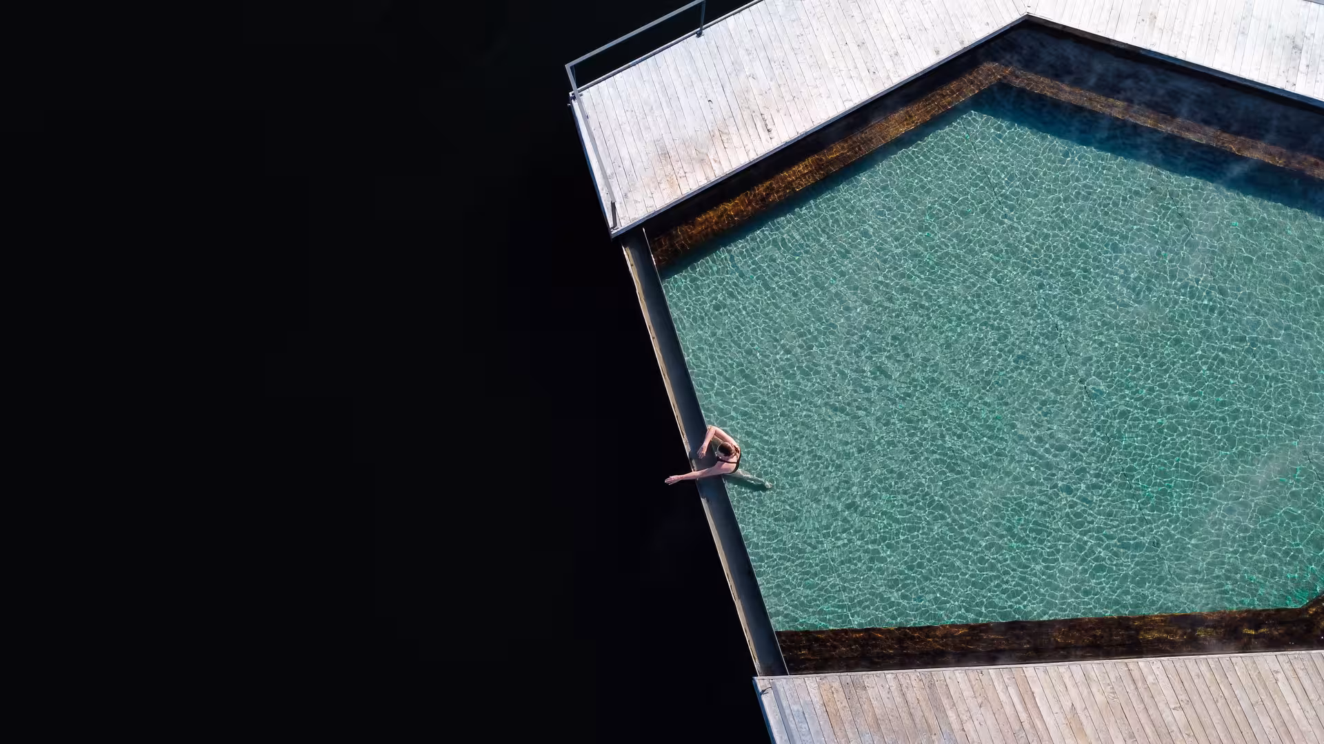 Aerial view of a person relaxing at the edge of Vok Baths geothermal floating pool in Eastfjords Iceland