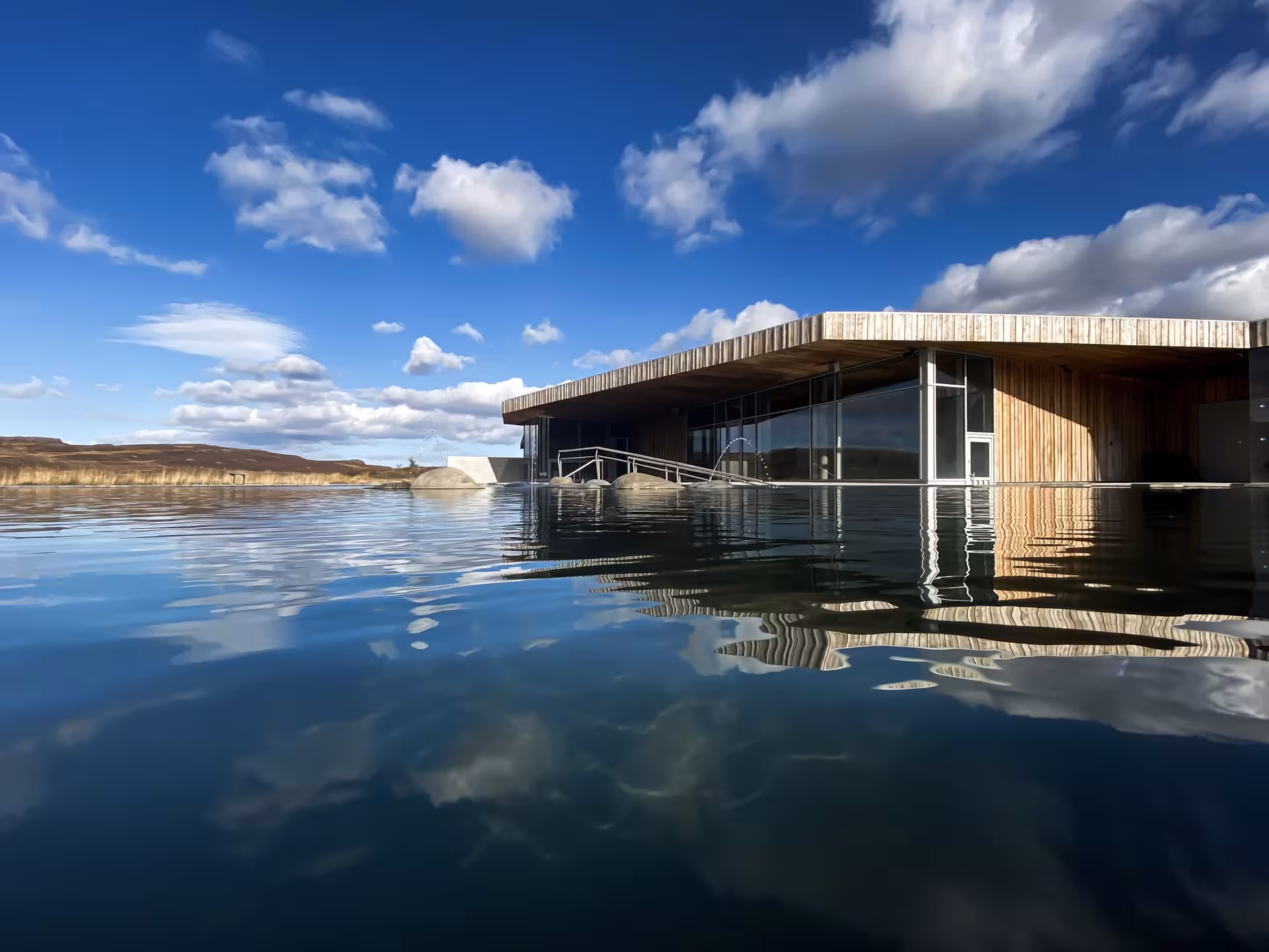 Vok Baths geothermal infinity pool with modern wooden pavilion reflecting in calm water, Eastfjords Iceland