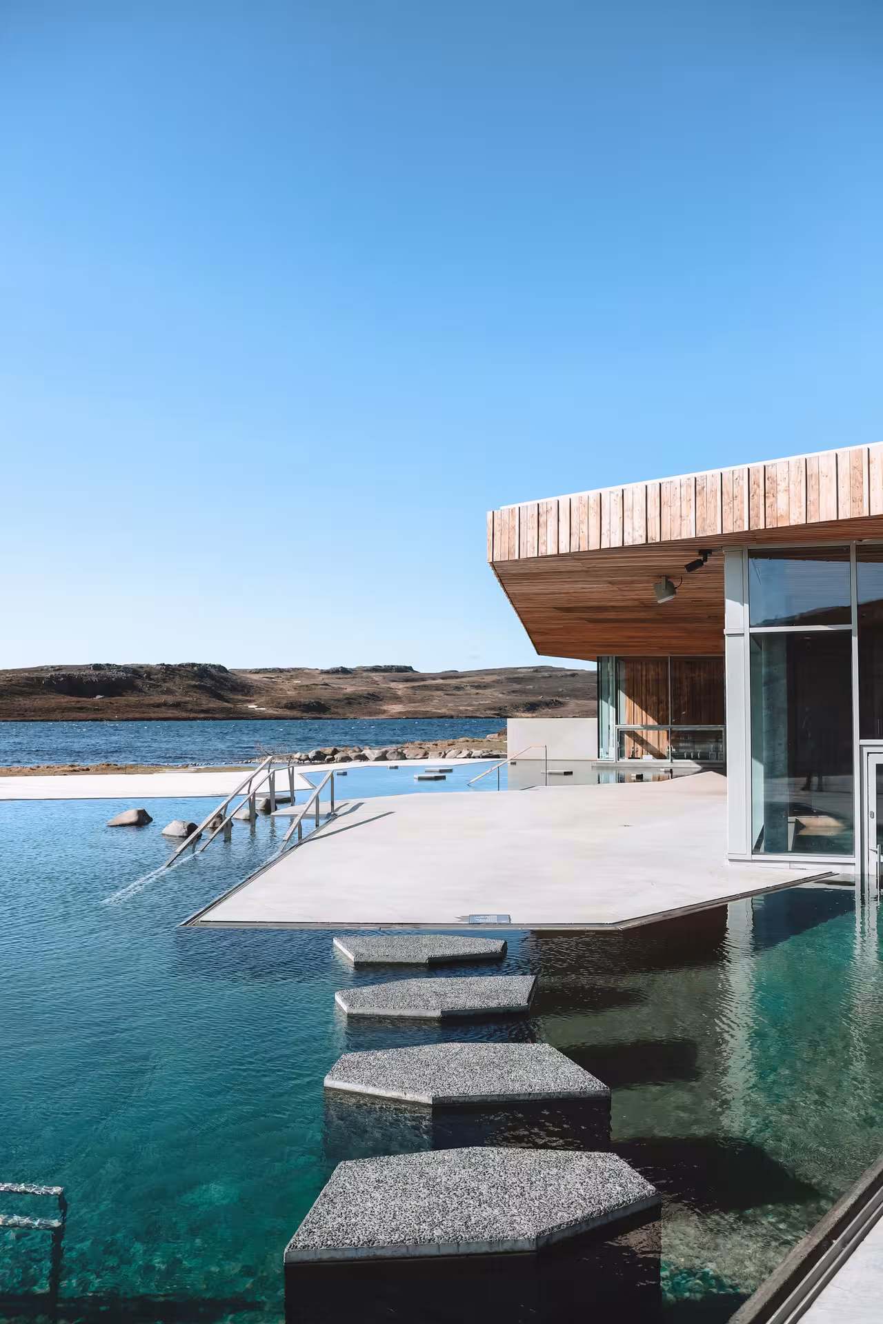 Vok Baths geothermal infinity pool with stepping stones and wooden pavilion overlooking East Iceland lake