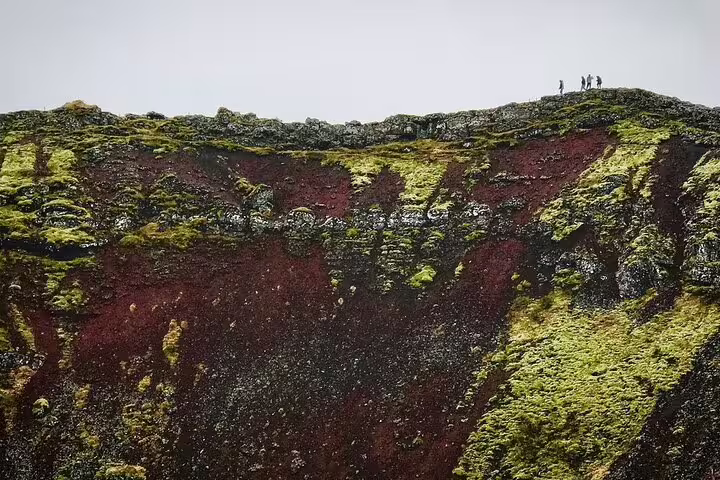 Hikers standing atop a volcanic crater ridge with red and black lava rock on the Golden Circle tour