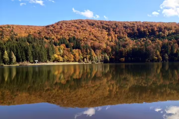 Autumn forest reflecting on a calm volcanic lake in Eastern Europe under a blue sky