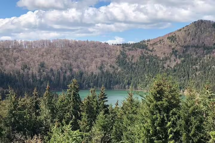 Turquoise volcanic lake surrounded by dense evergreen forest and hills in Eastern Europe