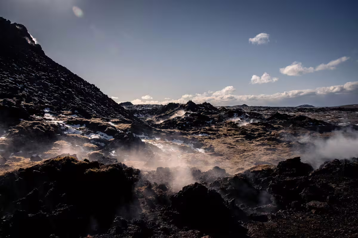 Steaming volcanic lava field with black rocks and geothermal vents under blue sky in Iceland