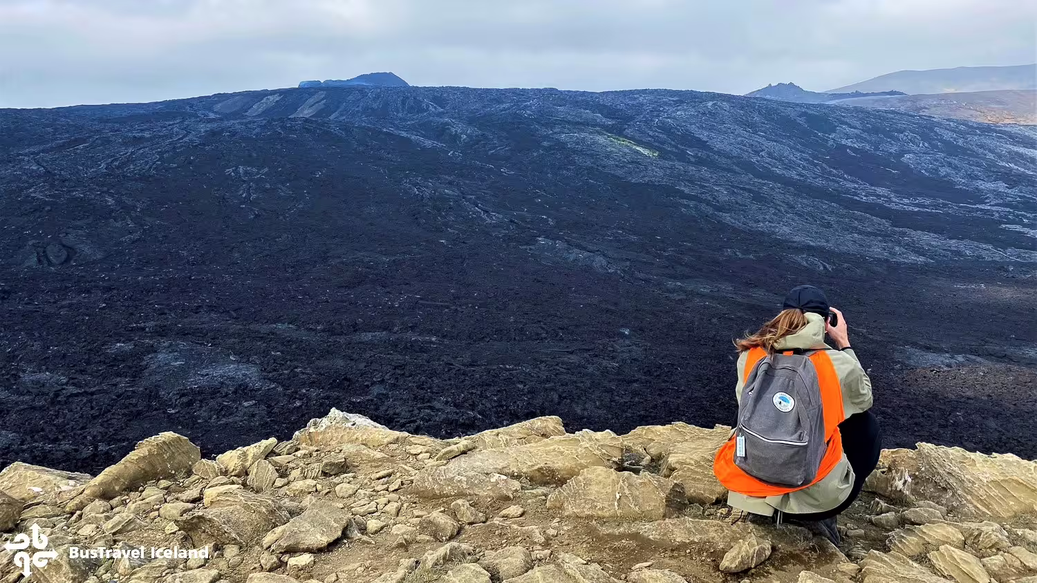 Hiker with backpack photographing vast black lava field on Iceland volcano hike near Reykjavik