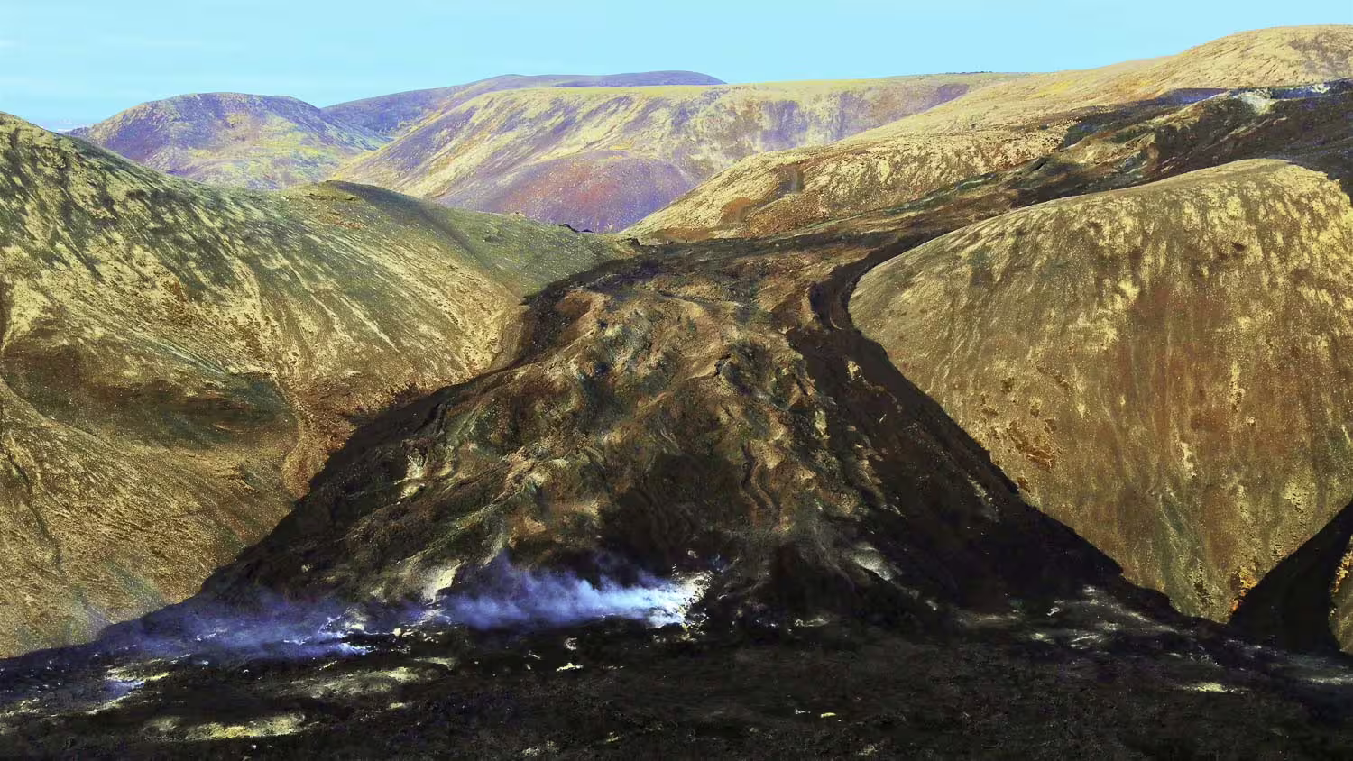 Steaming volcanic landscape with dark lava fields and colorful mountains near Reykjavik Iceland
