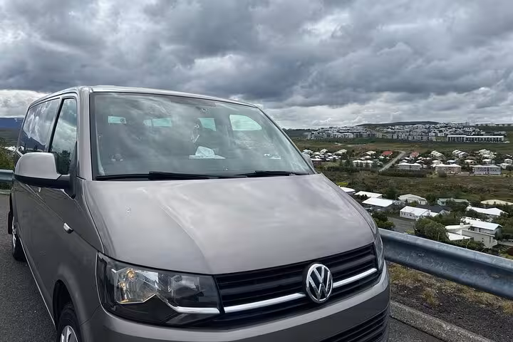 Gray Volkswagen Transporter minivan parked on Golden Circle private tour route in Iceland with town view